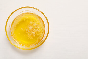 Melted butter in glass bowl on white wooden table, top view. Space for text