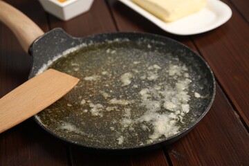 Melted butter in frying pan and spatula on wooden table, closeup