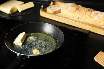 Melting butter in frying pan, dairy product and bread on black table