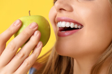 Young woman eating apple on yellow background, closeup