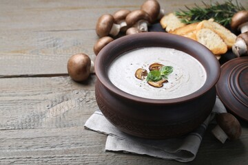 Delicious homemade mushroom soup in ceramic pot and fresh ingredients on wooden table. Space for text