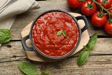 Homemade tomato sauce in bowl and fresh ingredients on wooden table, flat lay
