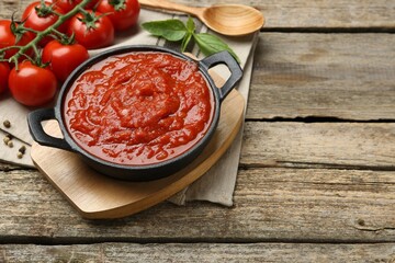 Homemade tomato sauce in bowl, spoon and ingredients on wooden table, space for text