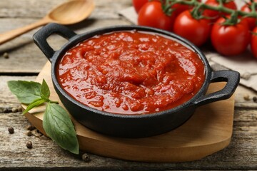 Homemade tomato sauce in bowl and basil on wooden table, closeup