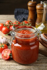 Homemade tomato sauce in jar and fresh ingredients on wooden table, closeup