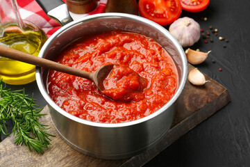 Homemade tomato sauce in pot, spoon and ingredients on dark table