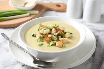 Tasty potato soup with croutons in bowl and spoon on white marble table