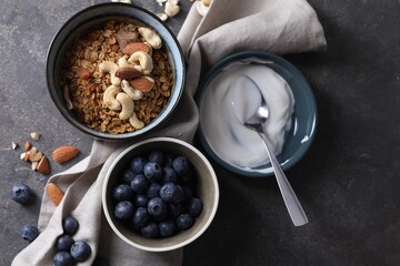 Tasty granola in bowl, blueberries, yogurt and spoon on gray textured table, flat lay