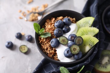 Tasty granola with yogurt, blueberries and kiwi in bowl on gray table, closeup