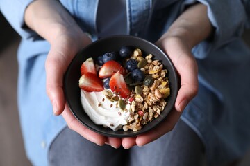 Woman holding bowl of tasty granola with berries, yogurt and seeds, top view