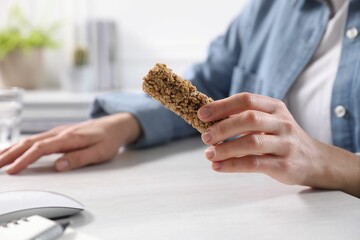 Woman holding tasty granola bar at light table indoors, closeup