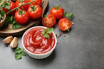 Delicious ketchup in bowl, tomatoes, parsley and garlic on grey table, closeup. Space for text