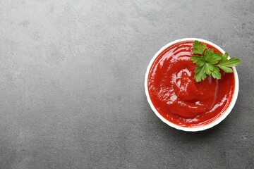 Delicious tomato ketchup and parsley in bowl on grey textured table, top view. Space for text