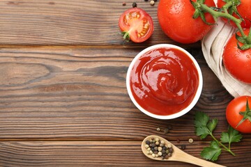 Delicious ketchup in bowl, tomatoes and peppercorns on wooden table, flat lay. Space for text