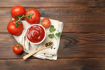 Delicious ketchup in bowl, tomatoes, parsley and peppercorns on wooden table, top view. Space for text