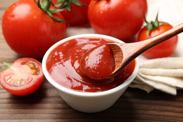 Taking delicious tomato ketchup with spoon from bowl at wooden table, closeup