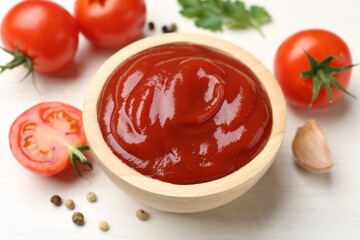 Delicious ketchup in bowl, garlic and tomatoes on white wooden table, closeup
