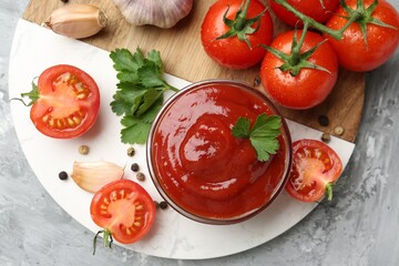 Delicious ketchup in bowl, parsley, garlic and tomatoes on grey textured table, top view