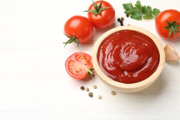 Delicious ketchup in bowl, peppercorns and tomatoes on white wooden table, above view. Space for text