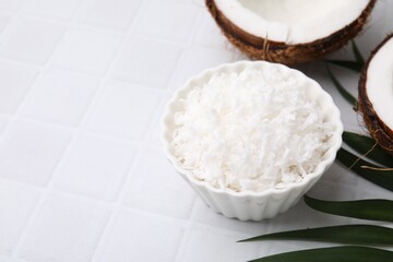 Coconut flakes in bowl, nuts and palm leaf on white tiled table, space for text