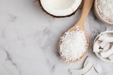 Coconut flakes, nut and spoon on white marble table, flat lay. Space for text