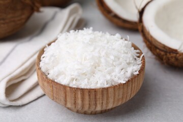 Coconut flakes in bowl and nut on light grey table, closeup
