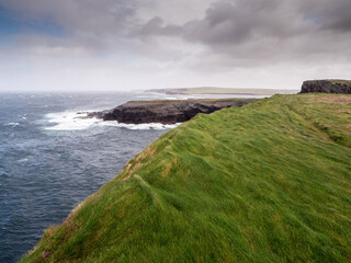 Kilkee cliff in county Clare, Ireland. Popular travel area with stunning nature scenery with green fields, ocean and dramatic sky. Irish landscape. Rough coast line. Warm sunny day.
