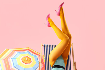 Legs of beautiful young woman with deckchair and umbrella on pink background