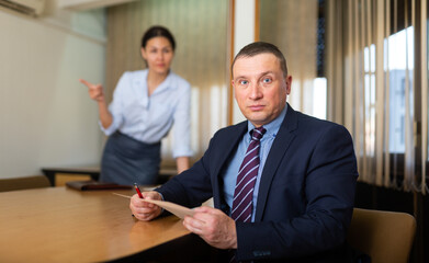 Portrait of upset businessman sitting with papers in hands at desk in office room with disgruntled...