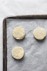 Overhead view of raw scones on a parchment lined baking sheet, top view of yogurt scones about to...