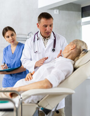 Fototapeta premium Male beautician, together with a nurse, examines the face of an elderly woman and plans facelift procedures.