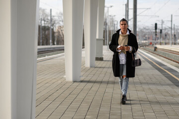 Trendy young woman in a coat walking on a train station towards camera