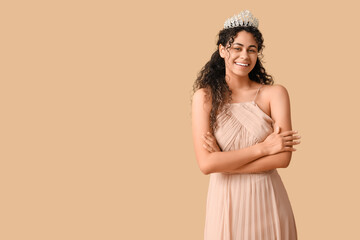 Beautiful young African-American woman in stylish beige prom dress and tiara on brown background © Pixel-Shot