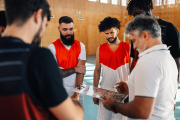 Diverse male basketball team and elderly coach discussing game tactics