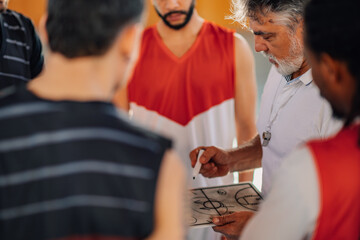 Diverse male basketball team and elderly coach discussing game tactics