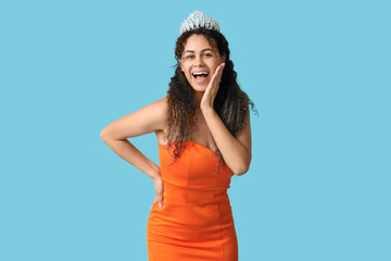 Happy young African-American woman in stylish orange prom dress and tiara on blue background © Pixel-Shot