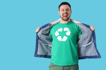Happy young man in t-shirt with recycling logo showing tongue on blue background. Ecology concept