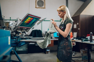 Print shop worker taking screen printed t-shirt off machine at facility