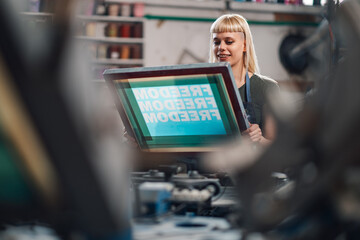 Graphic technician working with screen printing plate at print shop.