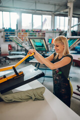 Print shop worker using heating press on textile product at facility.