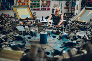Female graphic worker is screen printing on carousel printing machine.