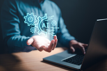 iot, machine, artificial, ai, brain, strategy, intelligence, robot, learning, innovation. A man is holding a laptop with a blue screen that has a picture of gears and the word AI.