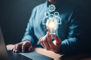 light bulb, communication, imagination, intelligence, invention, solution, strategy, teamwork, thinking, inspiration. A man is holding a light bulb in his hand and is typing on a laptop.