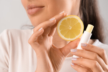 Young woman with lip balm and lemon on light background, closeup