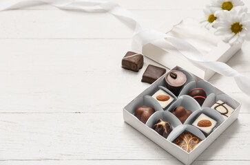 Box with tasty candies and chamomiles on wooden background