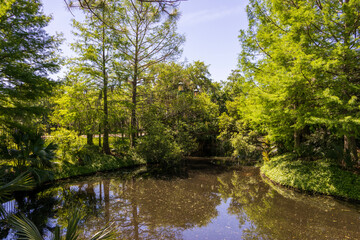 a beautiful spring landscape in the Sculpture Garden at New Orleans City Park with a lake, lush green trees, grass and plants, sculptures, people and blue sky in New Orleans Louisiana USA
