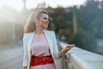 smiling stylish woman in pink dress and white jacket in city