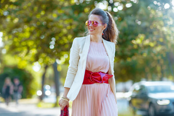 smiling stylish woman in dress and jacket in city walking