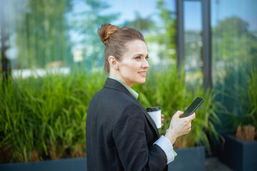 smiling woman worker near office building using smartphone