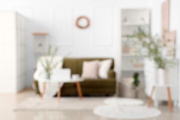 Stylish room with green sofa, coffee table and blooming branches, blurred view